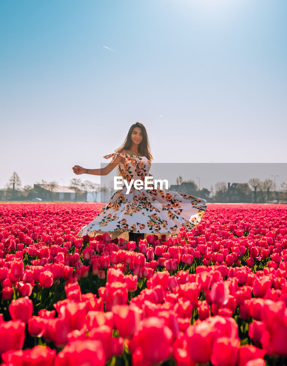 Woman standing by red flowering plants against sky