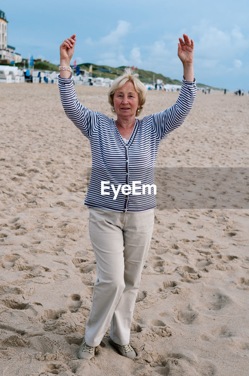 Portrait of senior woman with arms raised standing at beach