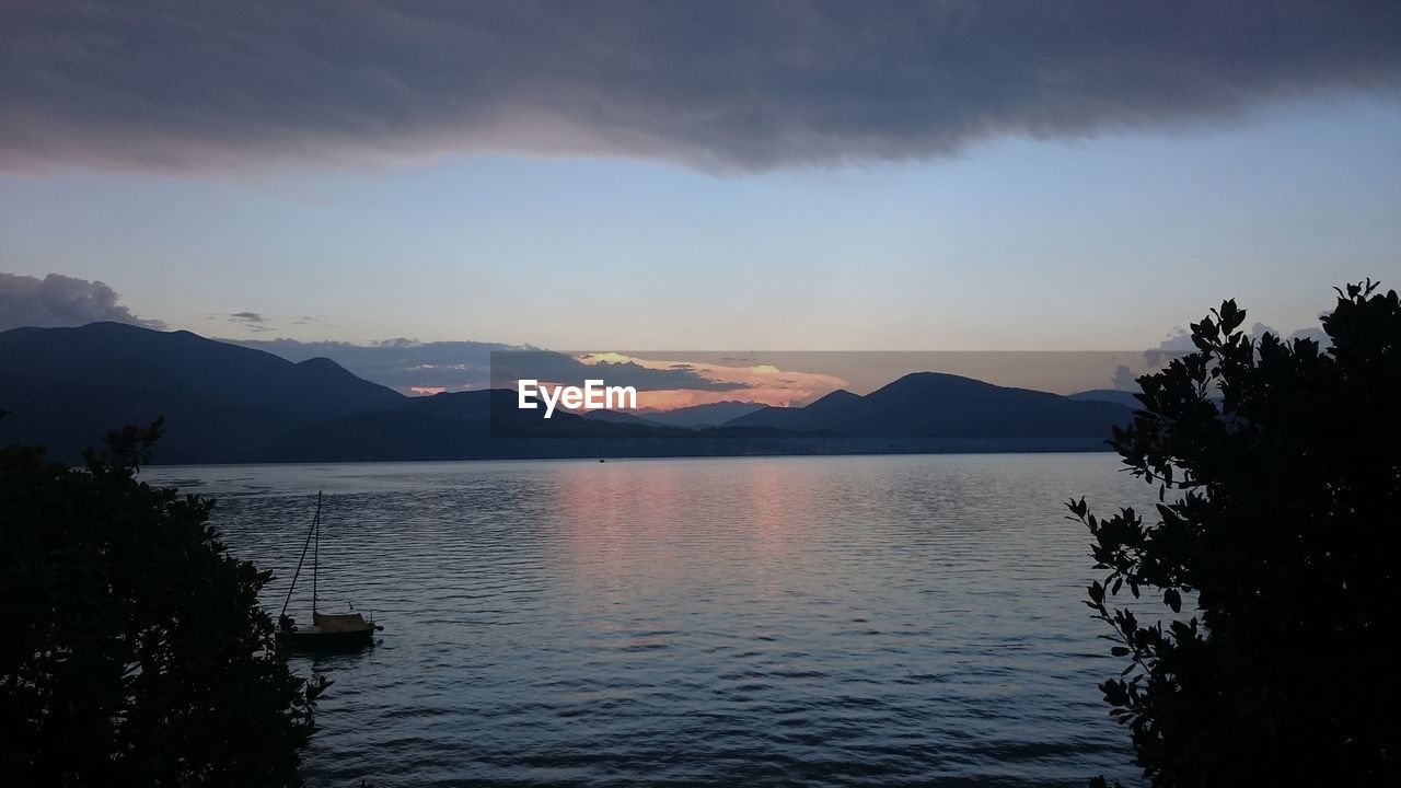 SCENIC VIEW OF LAKE BY SILHOUETTE MOUNTAINS AGAINST SKY AT SUNSET