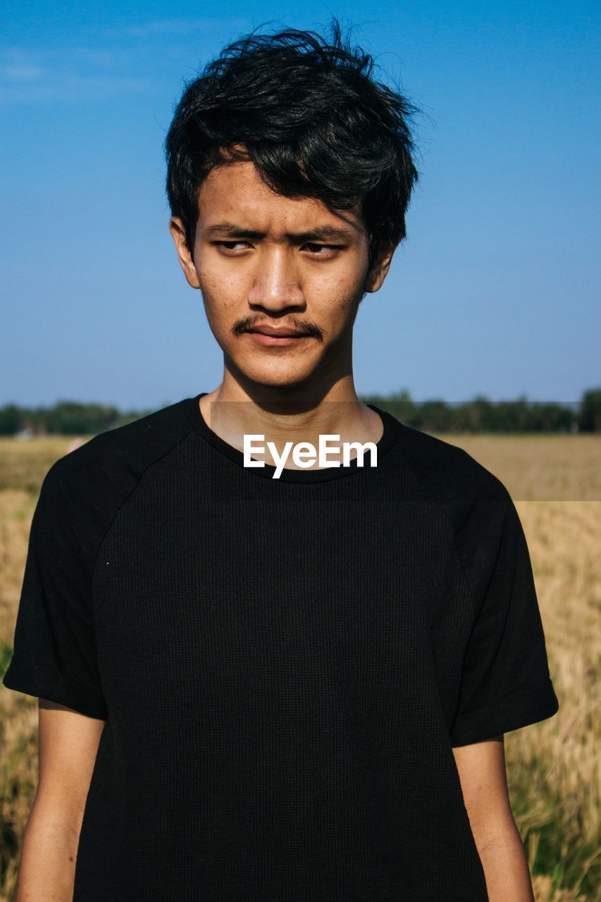 Young man looking away while standing on field