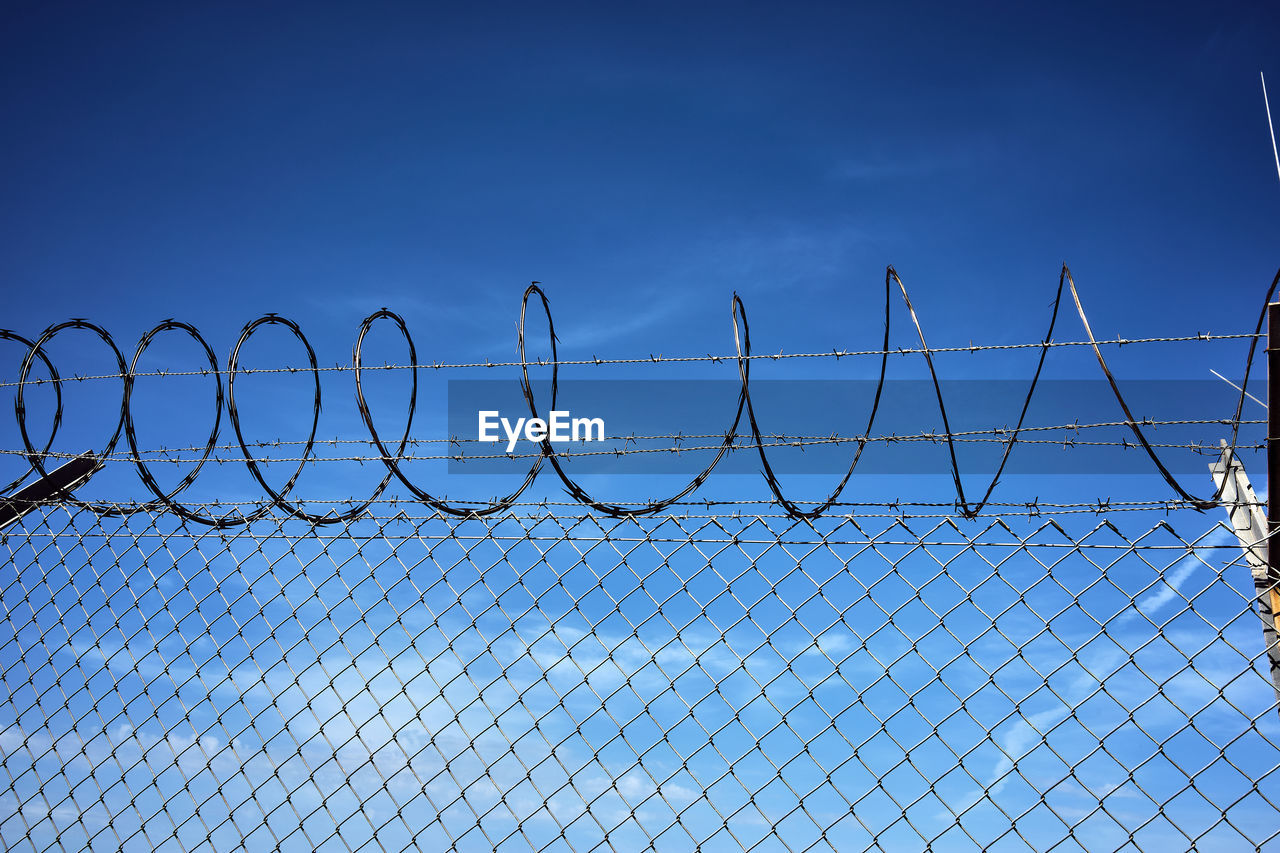 Low angle view of chainlink fence against blue sky