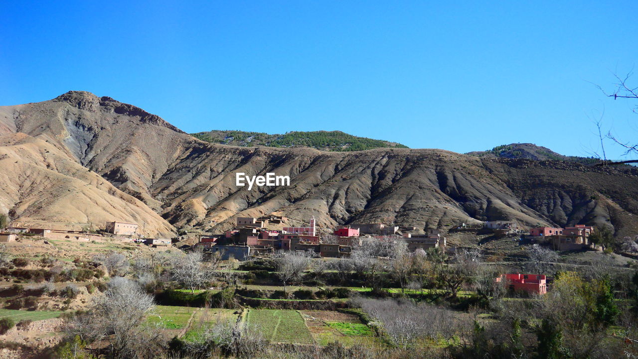 PANORAMIC SHOT OF HOUSES AND MOUNTAINS AGAINST CLEAR BLUE SKY