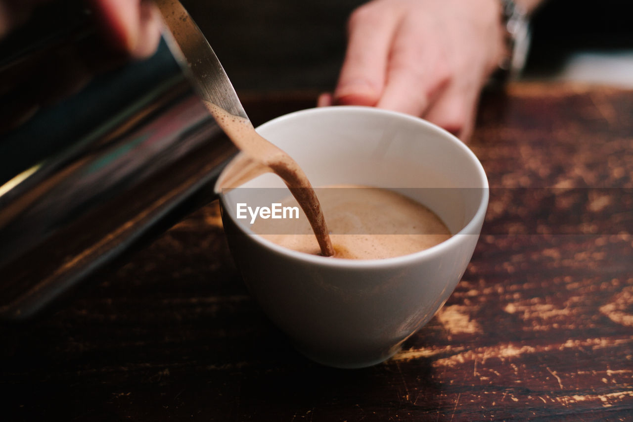 Cropped hands of person preparing coffee in cup on table