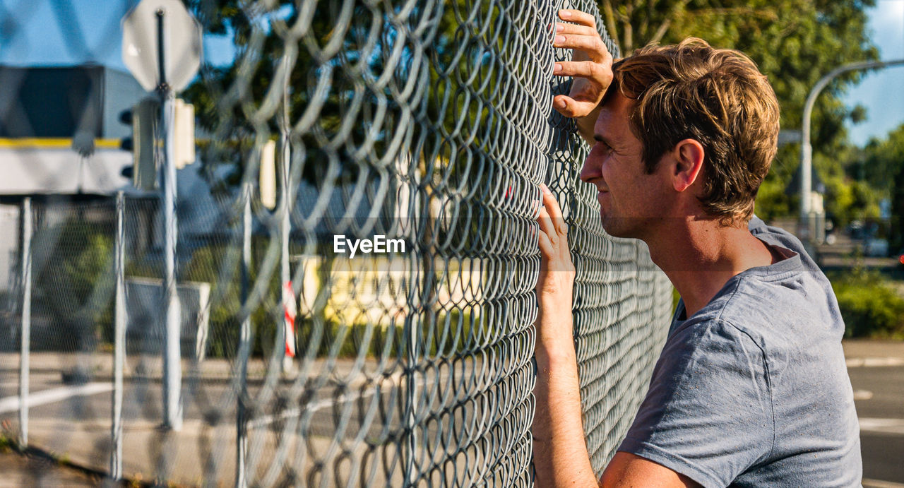 Caucasian man leaning forehead against outdoor fence deep in thought. profile view.