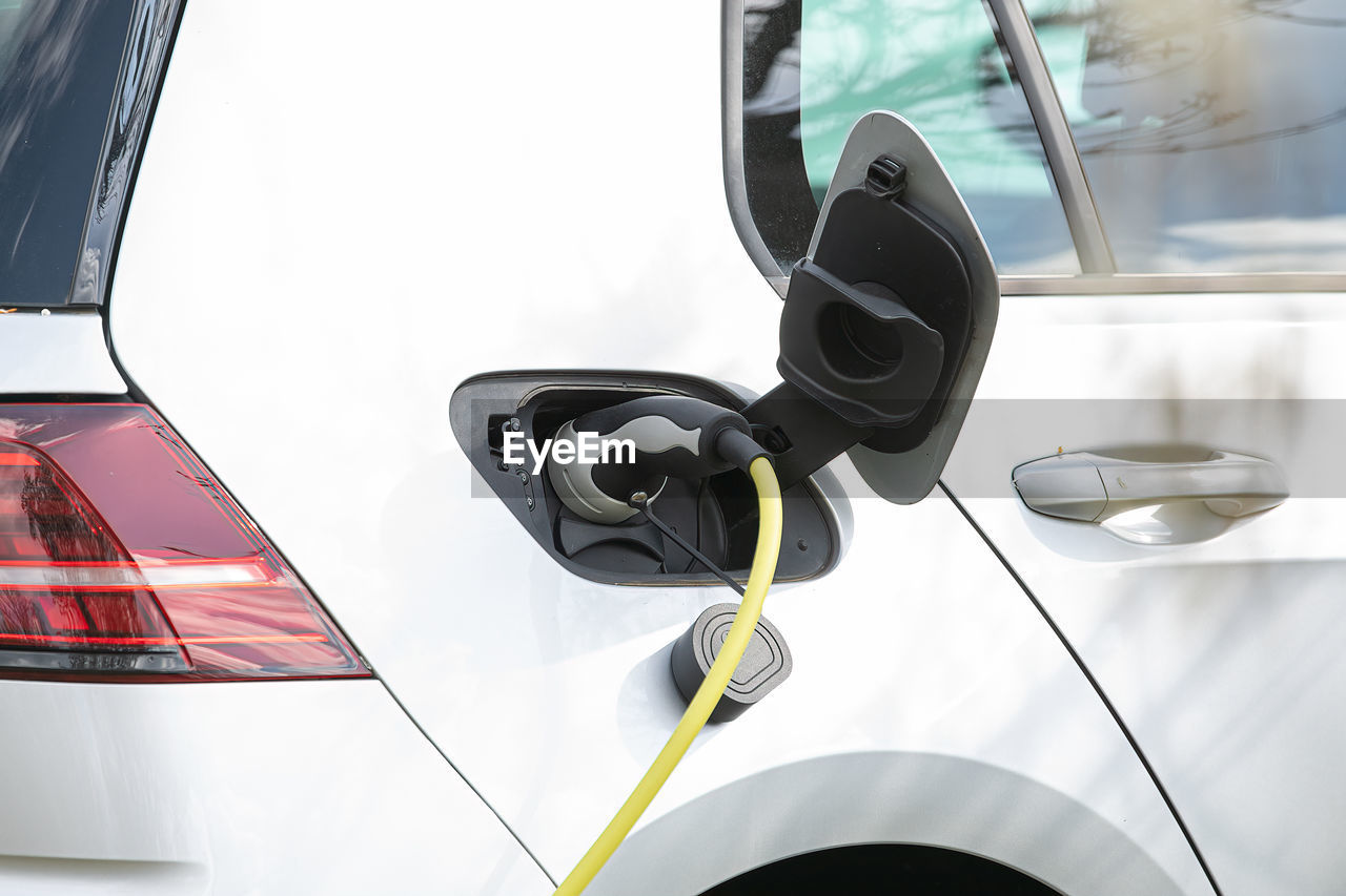 Plug in adapter in car charge battery of electric car next to a charging station with yellow cable 