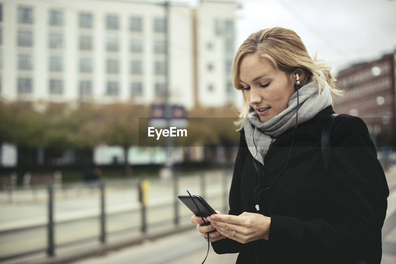 Mid adult businesswoman listening music through smart phone at tram station