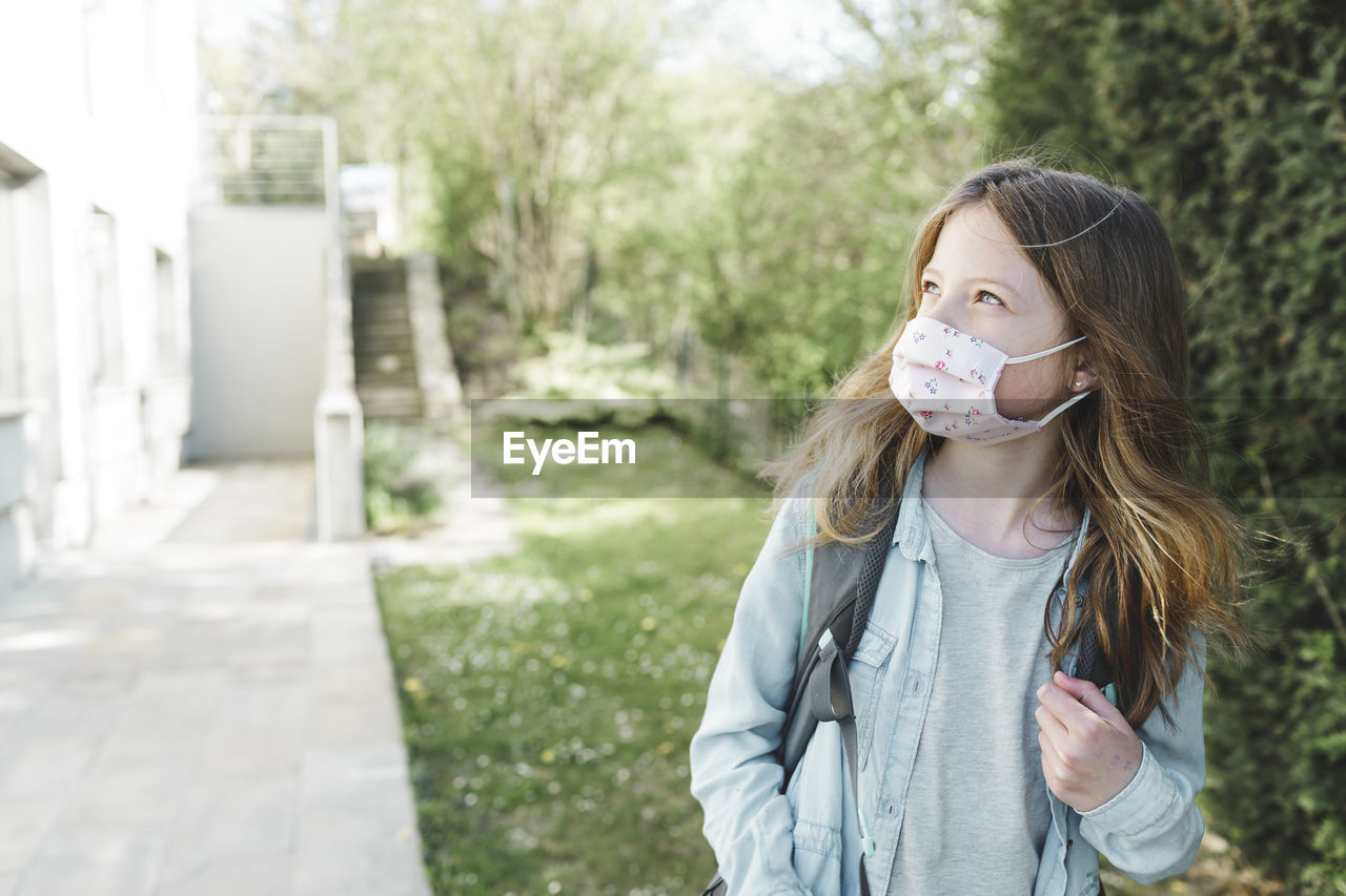 Girl wearing mask while standing with backpack