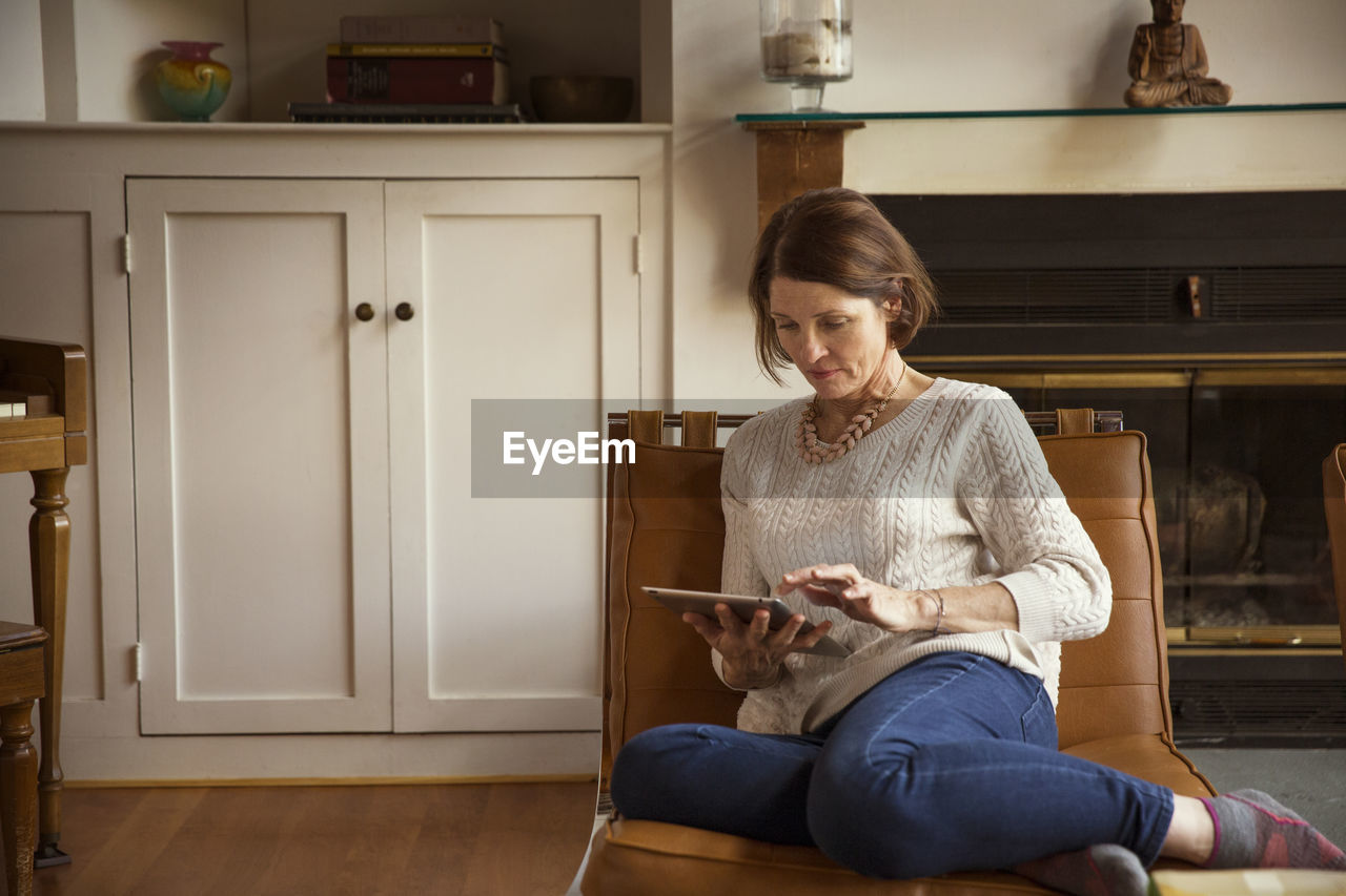 Woman using tablet computer while sitting on chair in living room