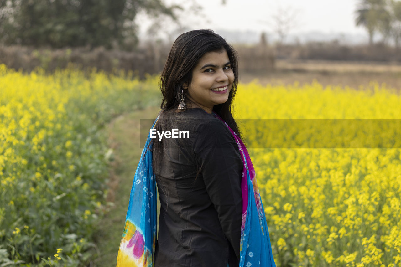 A pretty indian woman with smiling face looking back in mustard field