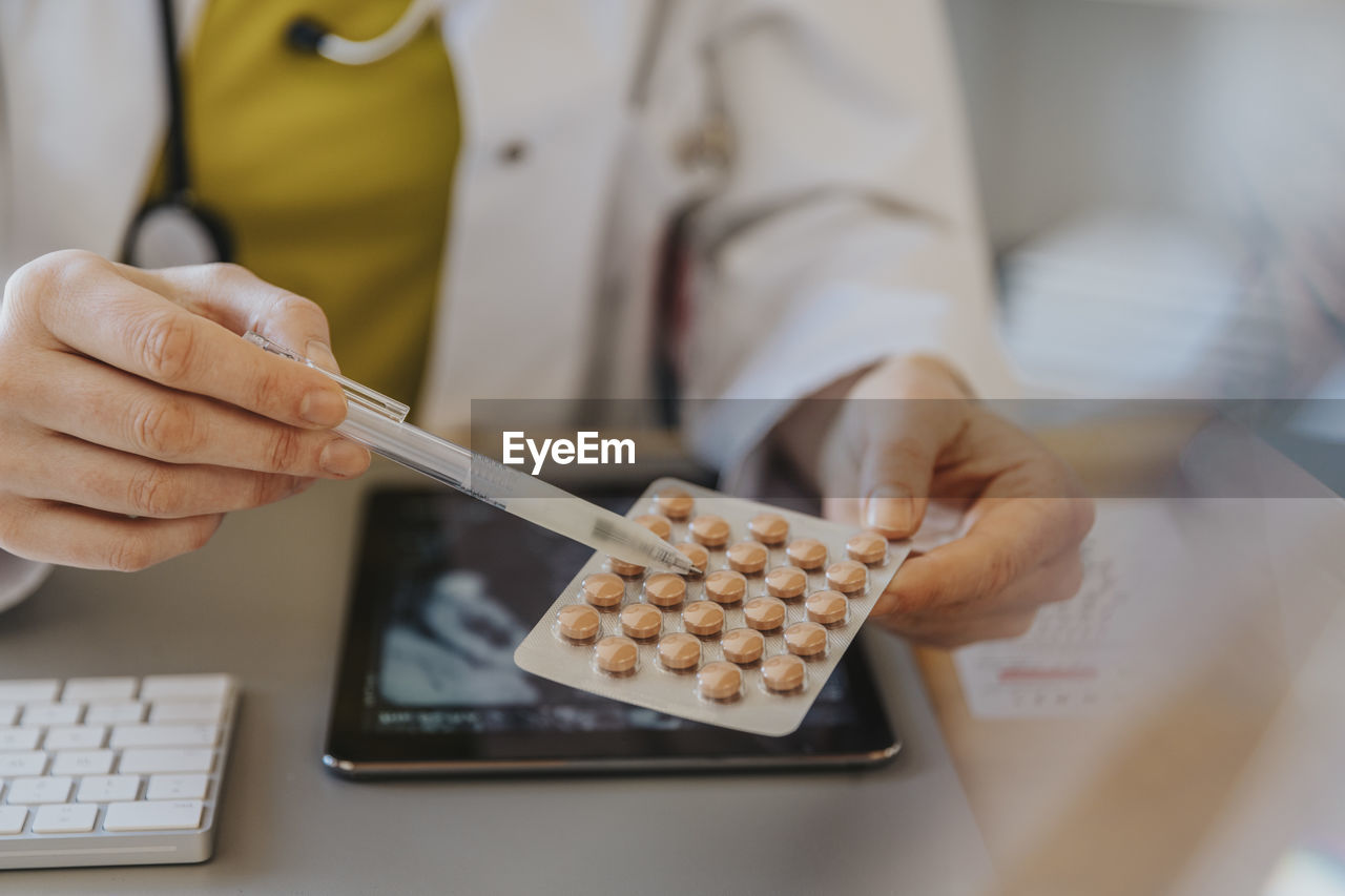 Doctor pointing at medicine while sitting by desk at clinic