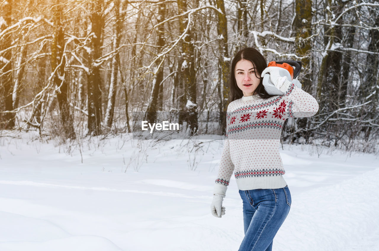 Portrait of woman holding chainsaw on snow field
