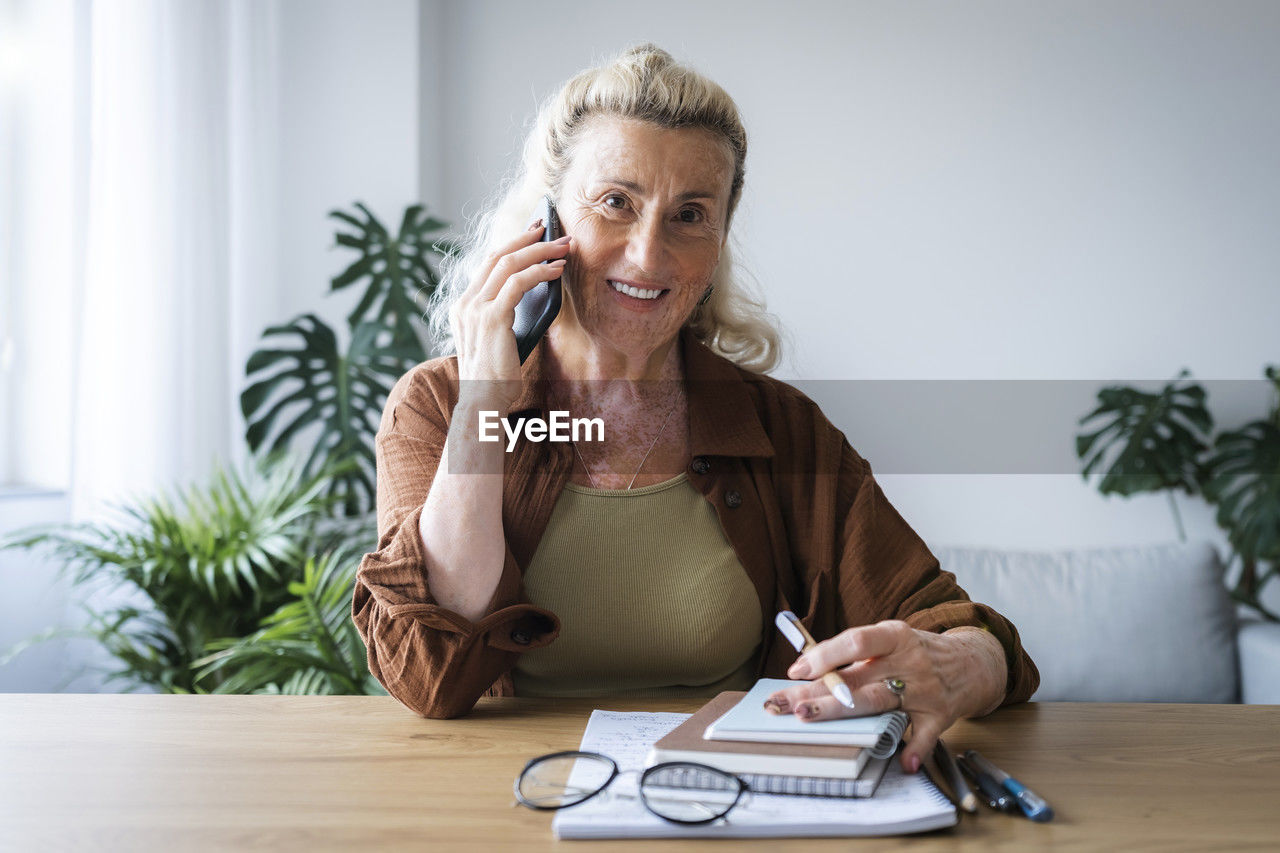 Smiling businesswoman talking on mobile phone at home office