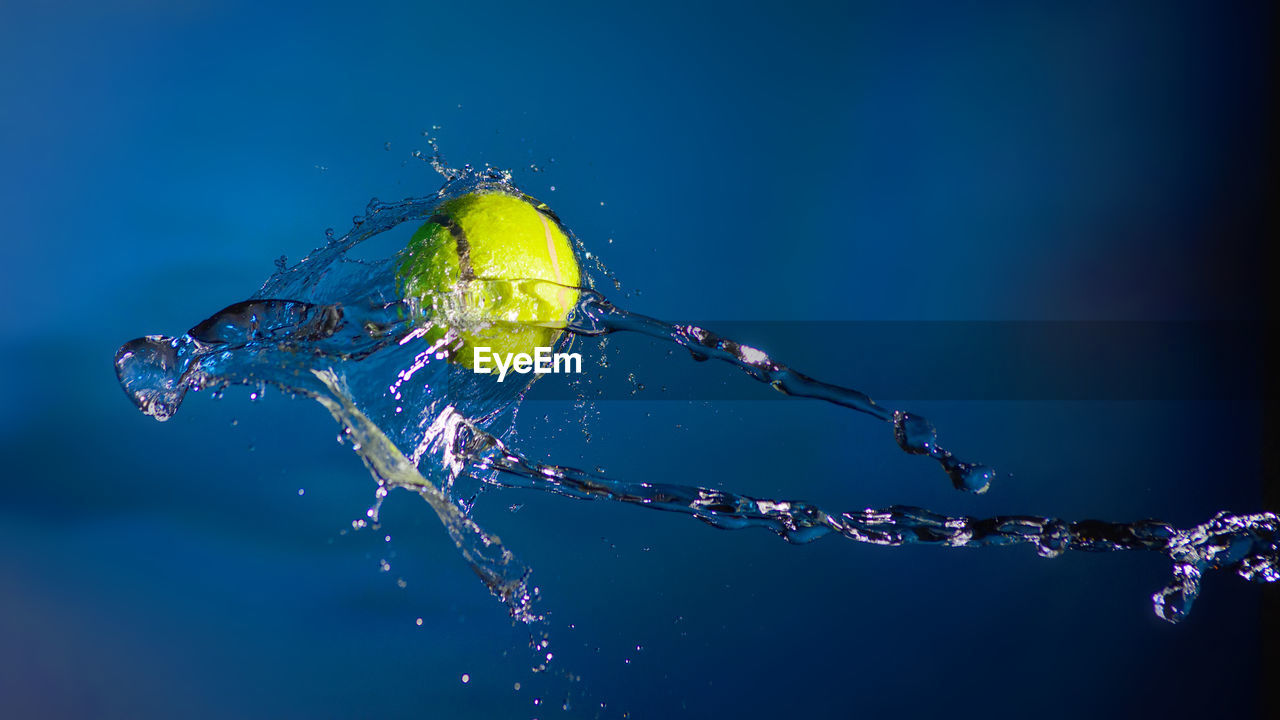 Tennis ball and splashes of water on a blue background.