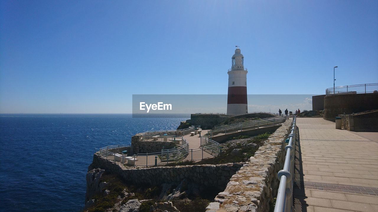 LIGHTHOUSE AMIDST SEA AND BUILDINGS AGAINST SKY