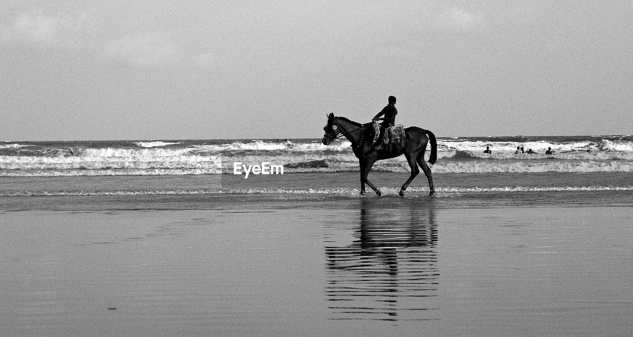 Side view of a man riding horse on beach