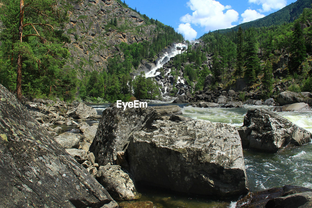 Alpine waterfall uchar in altai with huge stones and trees