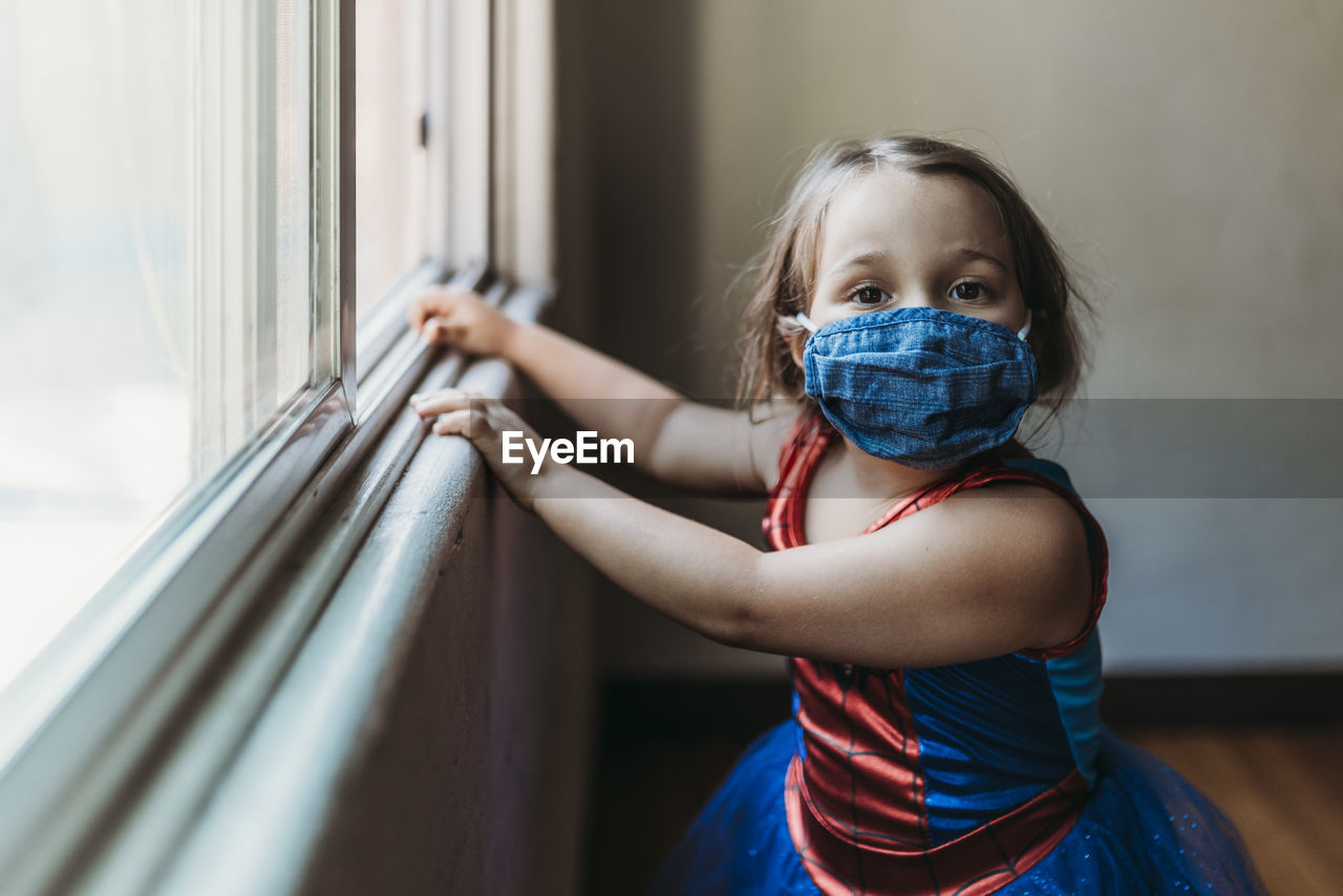 Preschool age girl by window in halloween costume and face mask