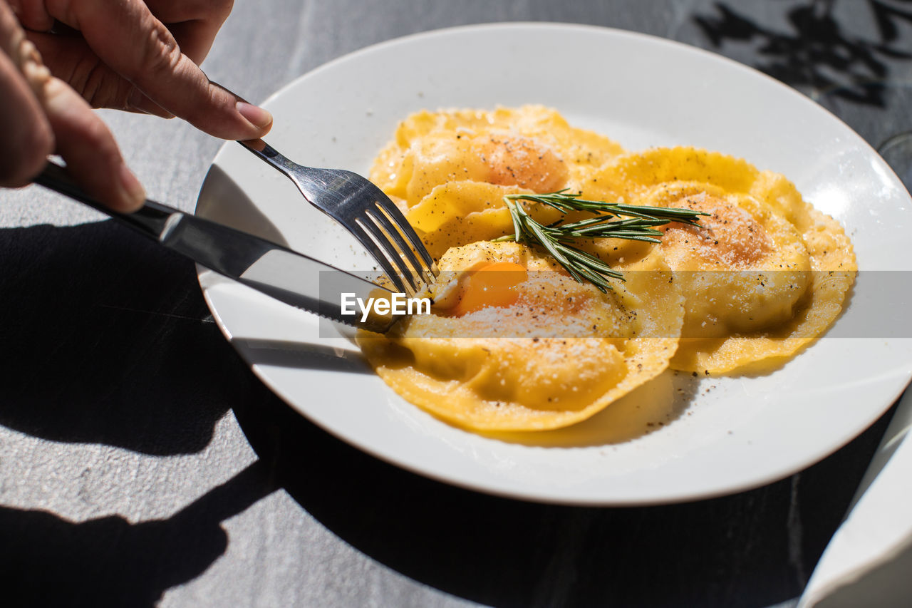 Cropped image of person having fried egg in plate on table