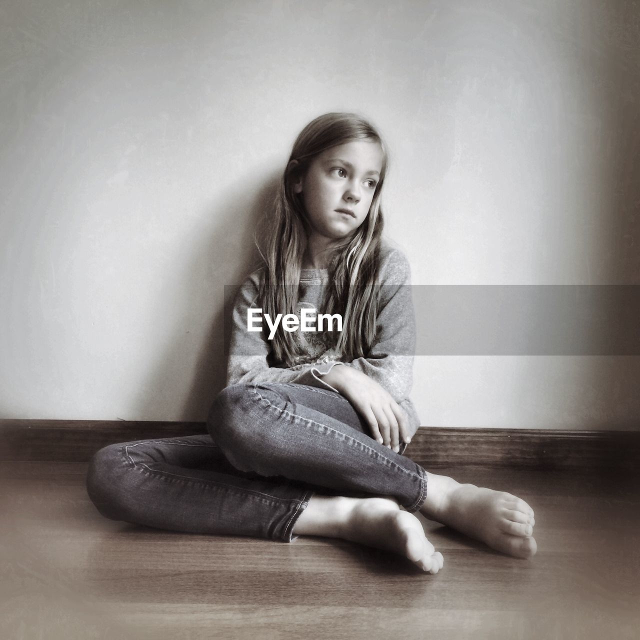 Full length of a sad girl sitting on floor against wall