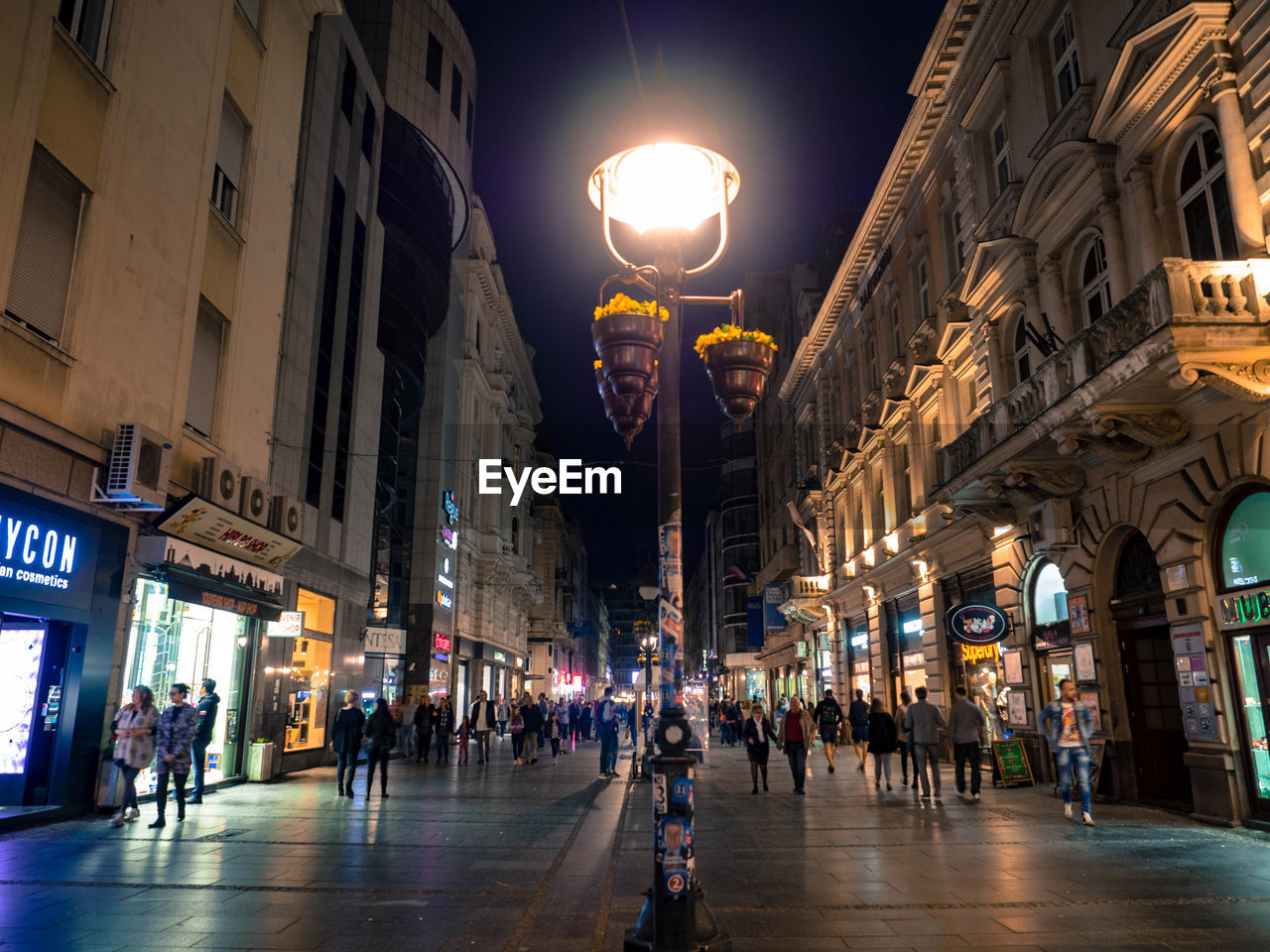 PEOPLE WALKING ON STREET AMIDST ILLUMINATED BUILDINGS AT NIGHT