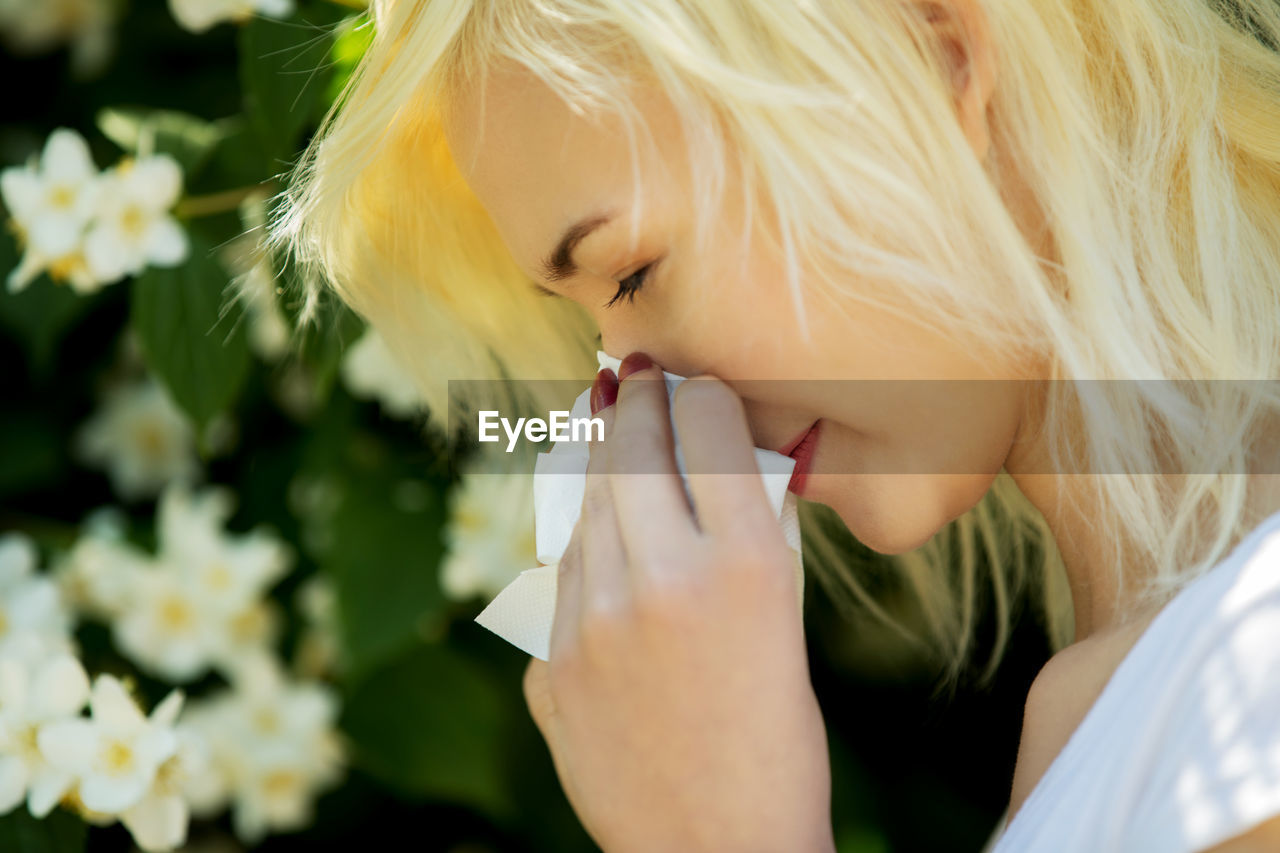 Close-up of teenage girl blowing nose in tissue outdoors