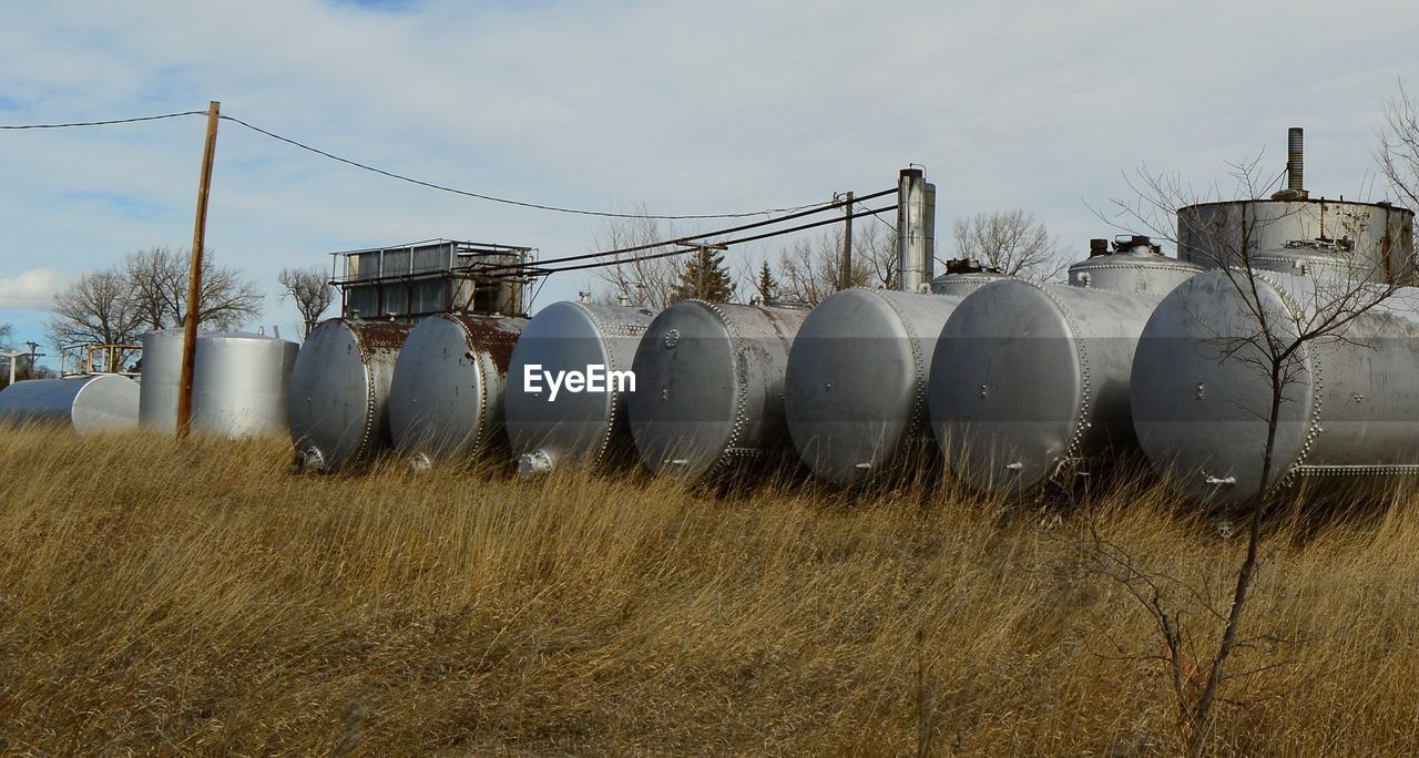 Silver storage tanks on grassy field against sky
