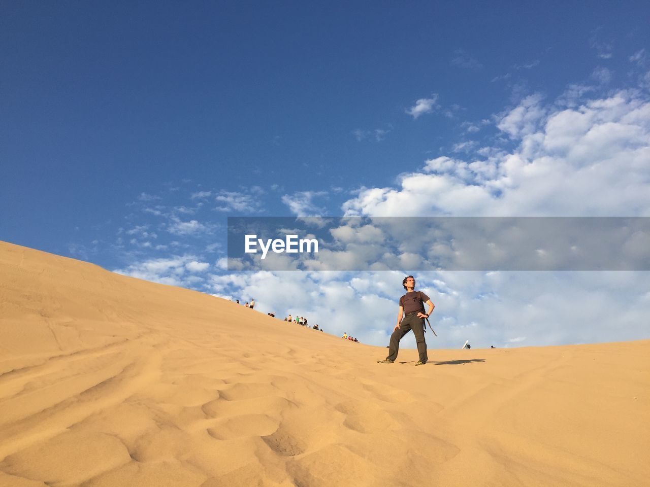 Low angle view of man standing on sand dune in desert against sky