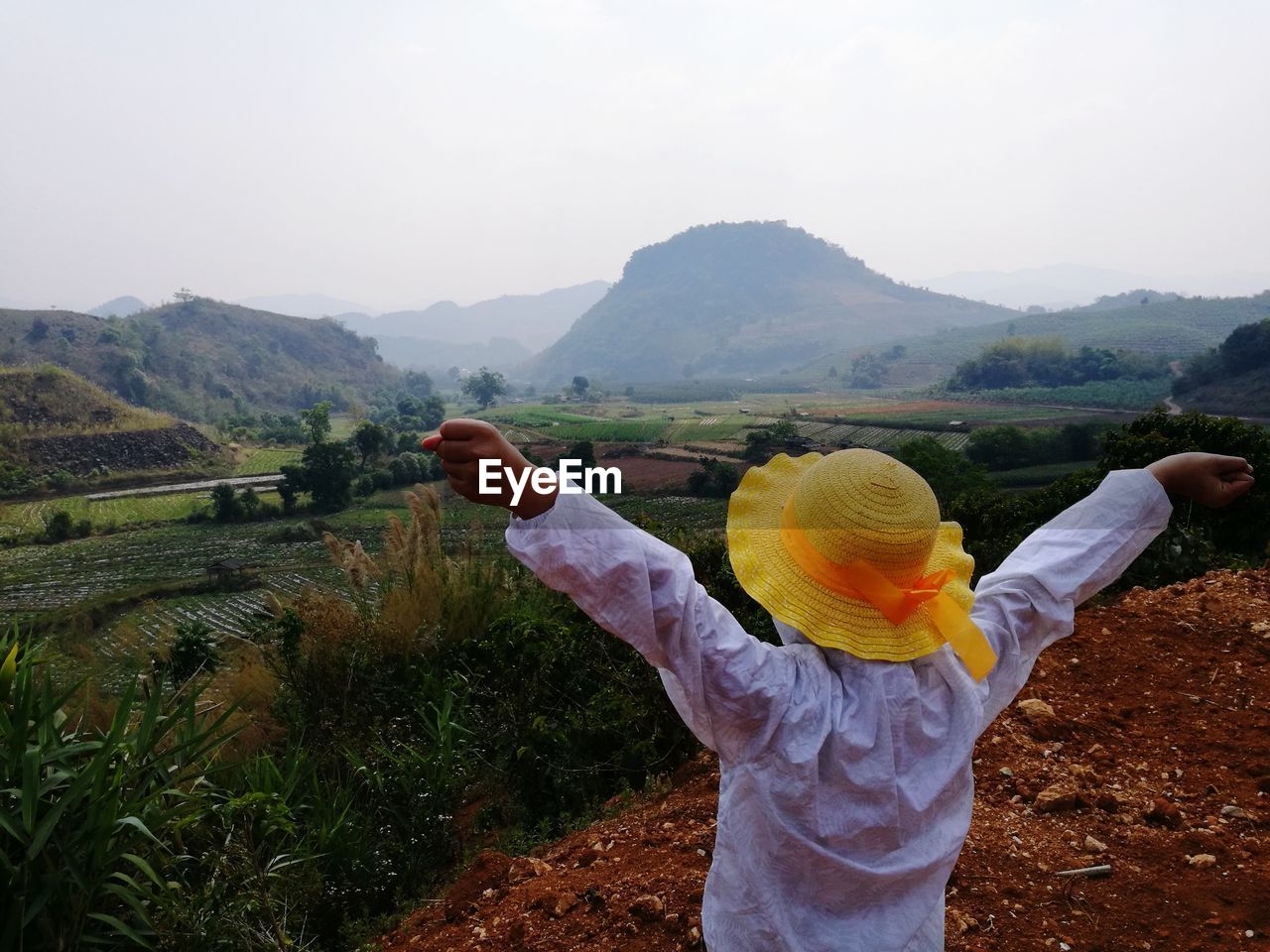 Rear view of woman with arms raised standing on field against sky