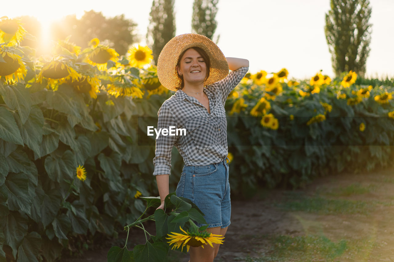 Beautiful young woman with sunflowers enjoying nature and laughing on summer sunflower field.