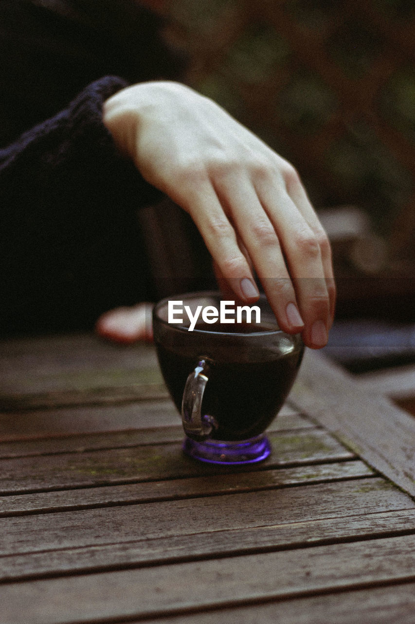 Cropped hand of woman with coffee on wooden table in cafe