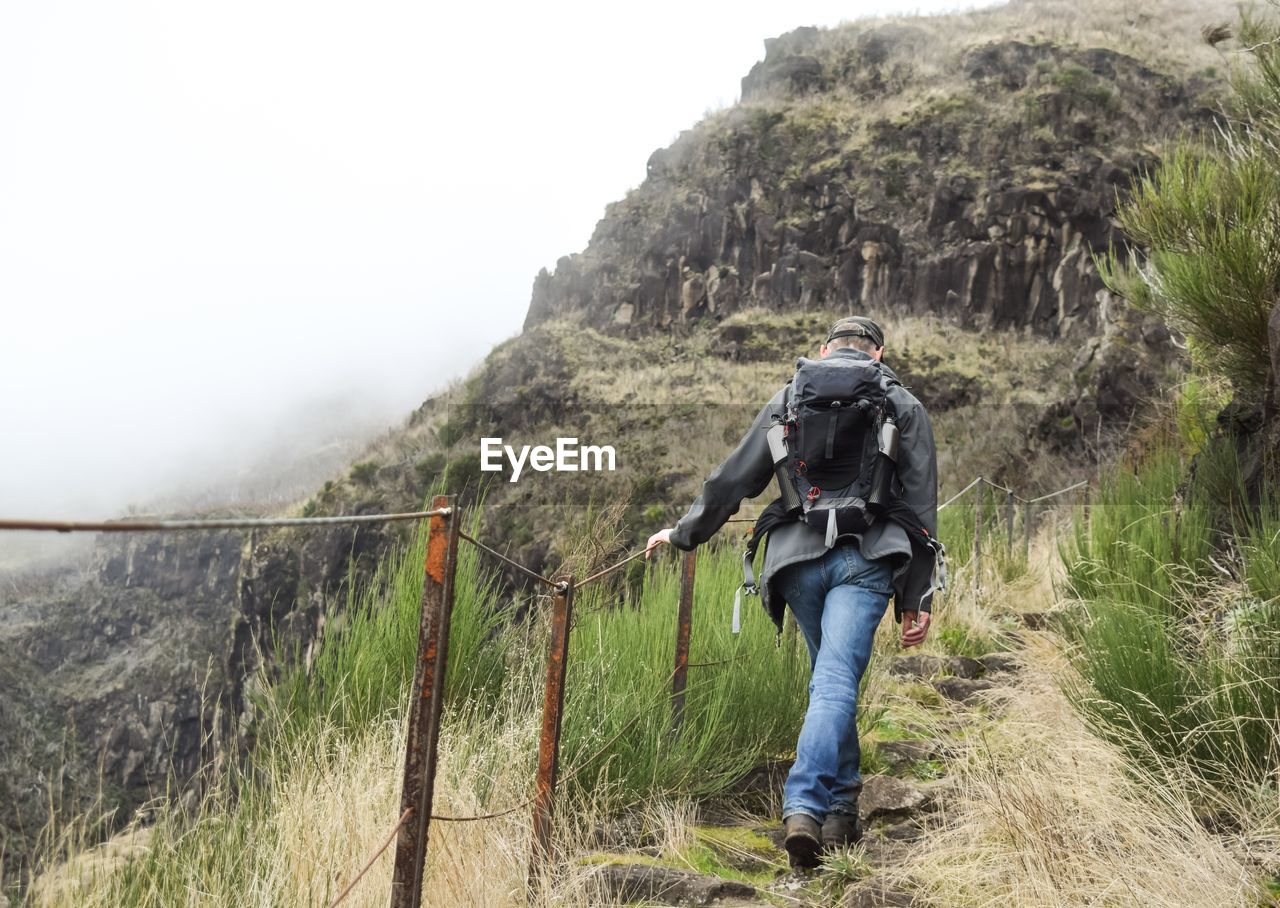 Rear view of man walking on mountain against sky