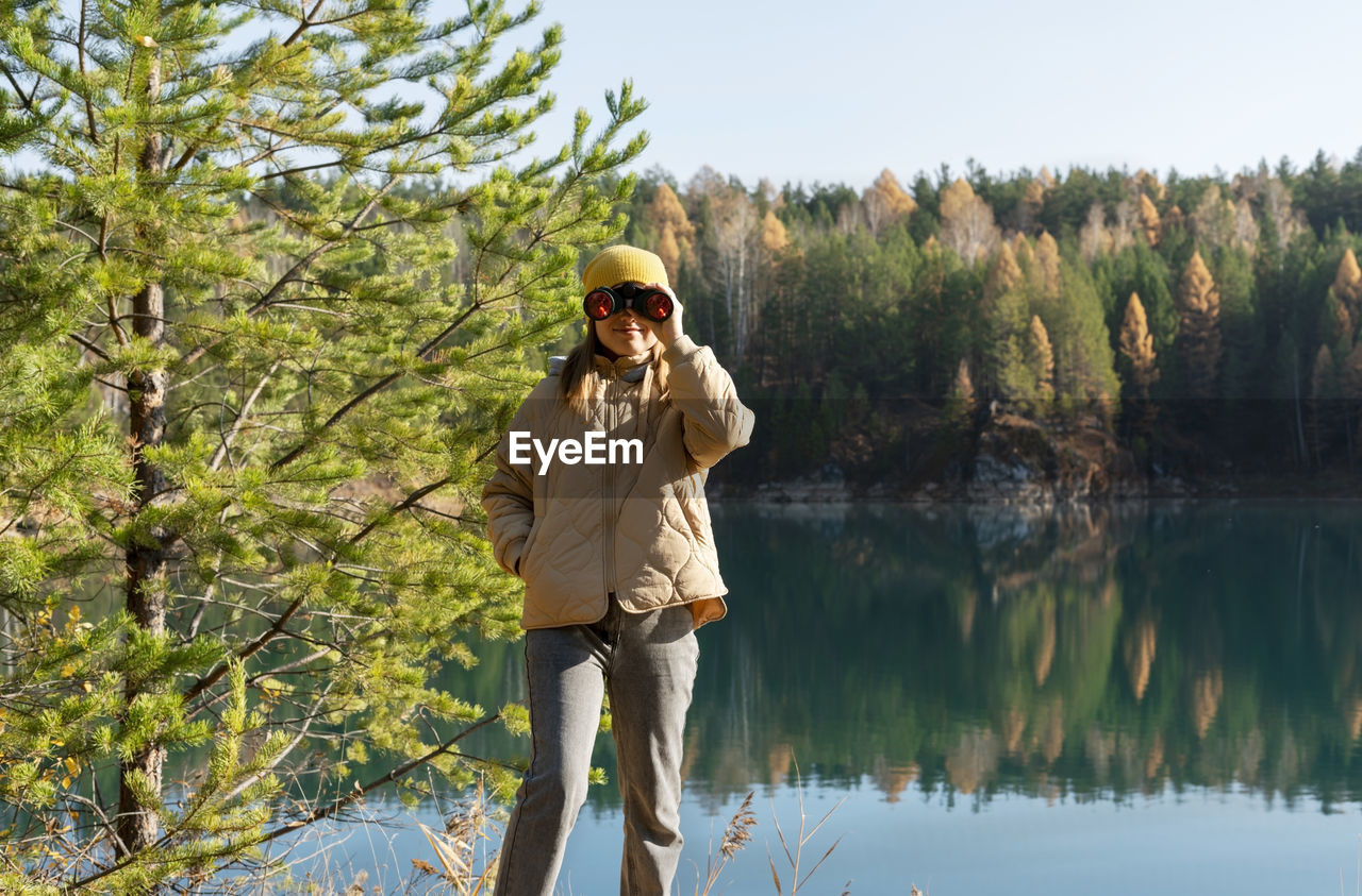 full length of young woman standing against lake