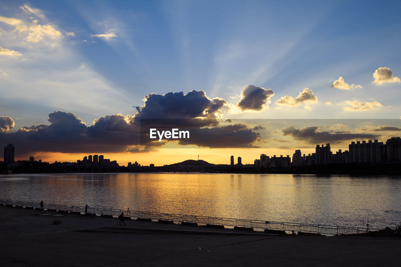 SCENIC VIEW OF RIVER BY CITY AGAINST SKY DURING SUNSET