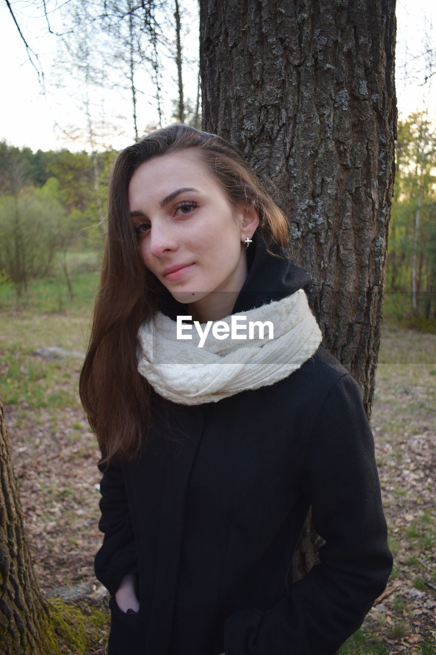 Portrait of young woman standing by tree