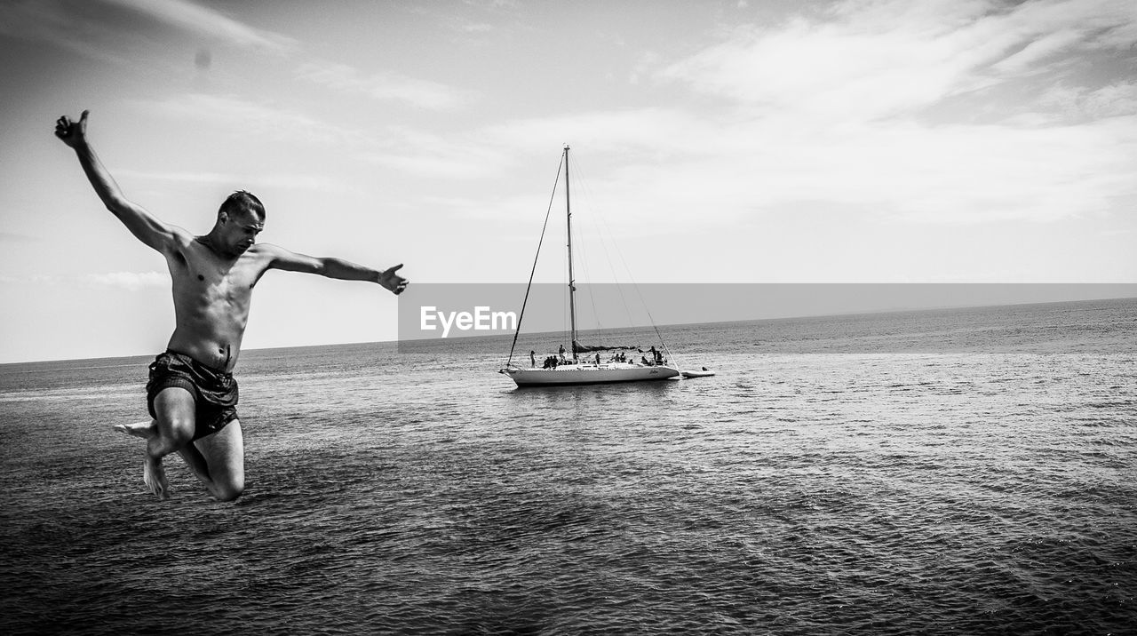 Man diving into sea with boat in background
