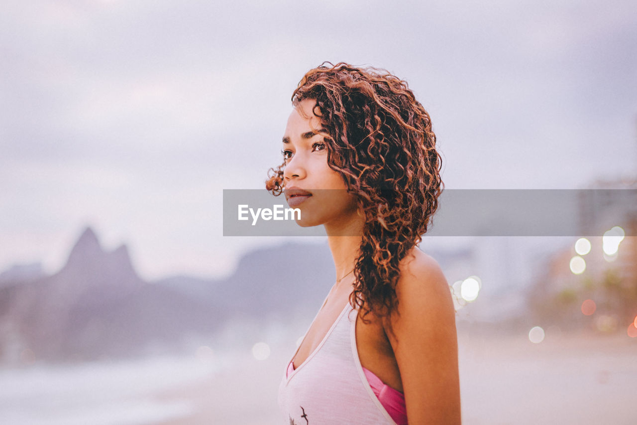 Close-up of young woman looking away at beach during sunset