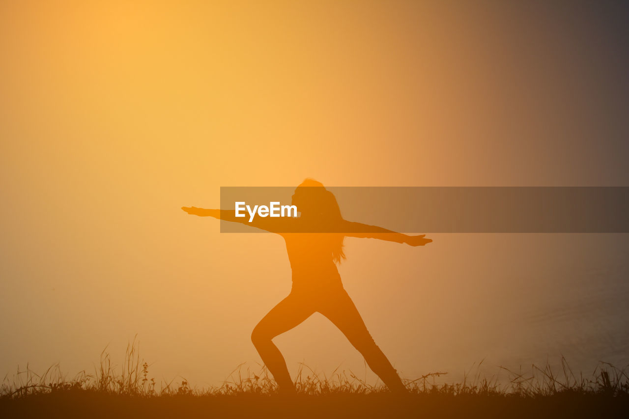 Silhouette woman exercising warrior 2 on field