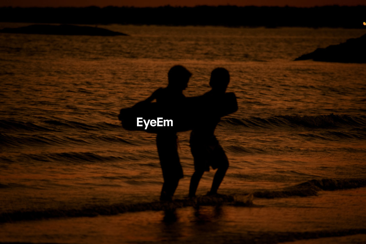 Silhouette boys standing on beach during sunset