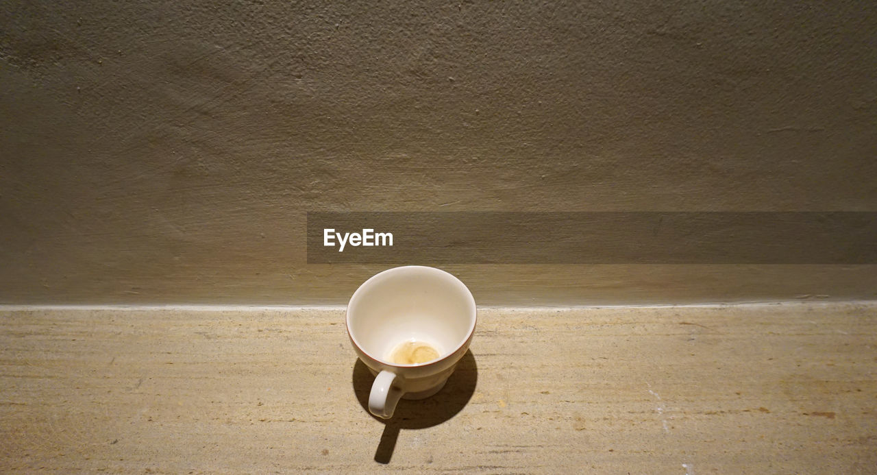 HIGH ANGLE VIEW OF EMPTY COFFEE CUP ON TABLE AGAINST WALL