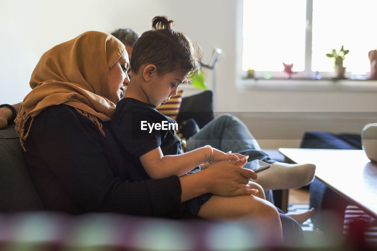 Side view of mother and son using digital tablet while sitting on sofa at home