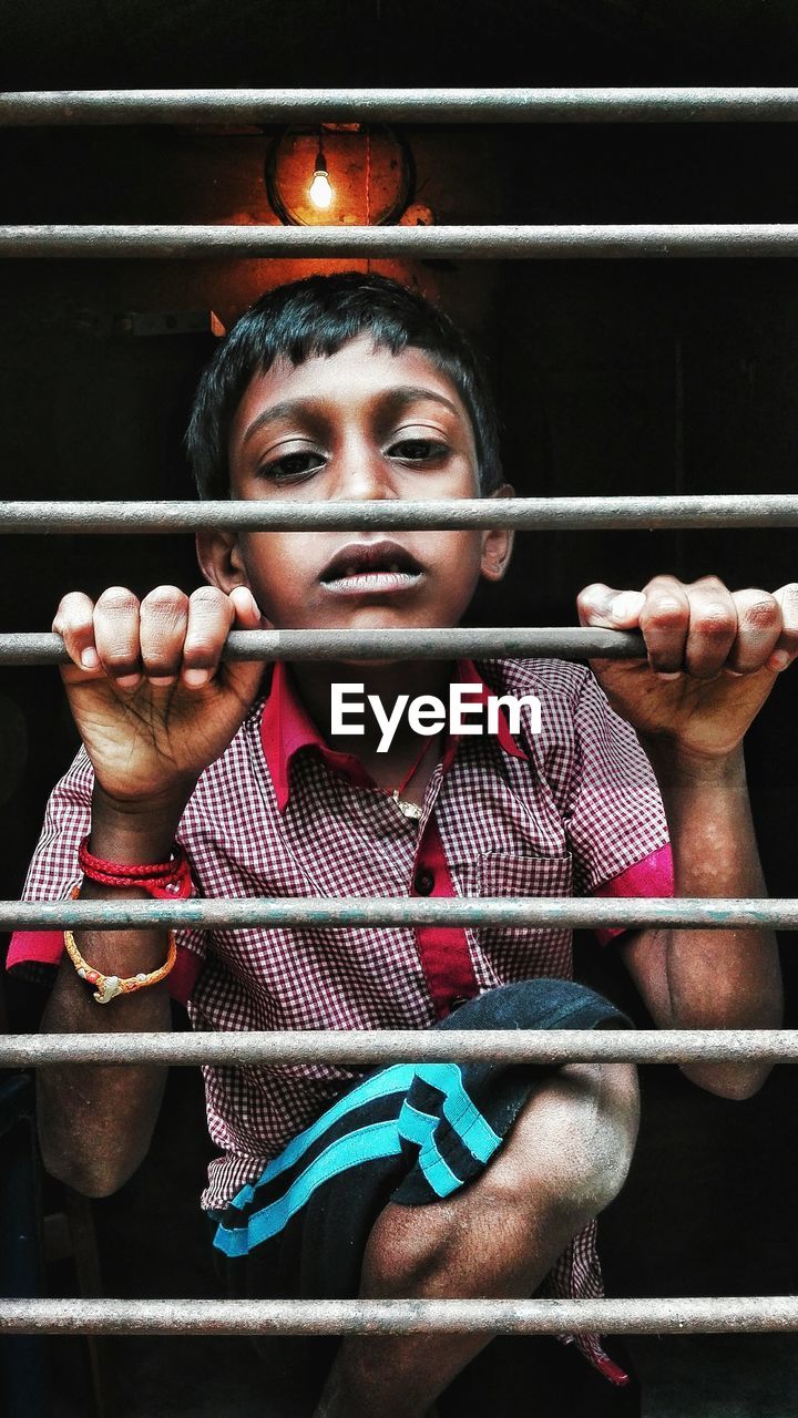 Portrait of boy holding security bars on window