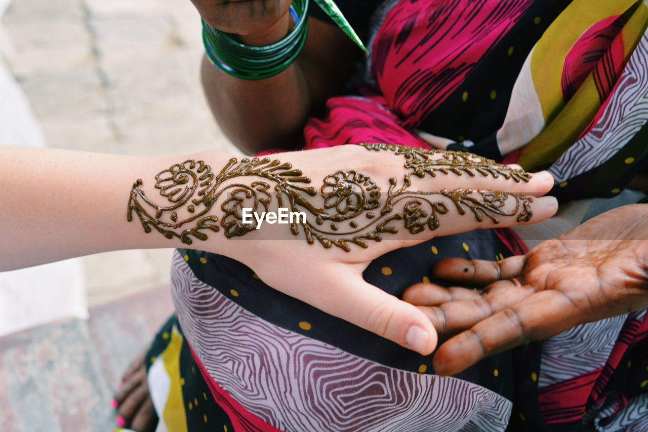 Midsection of woman applying henna tattoo on customer hand