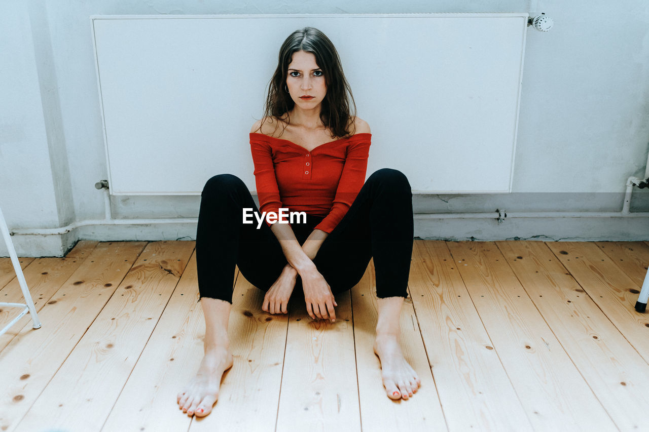 Full length portrait of young woman sitting on hardwood floor at home