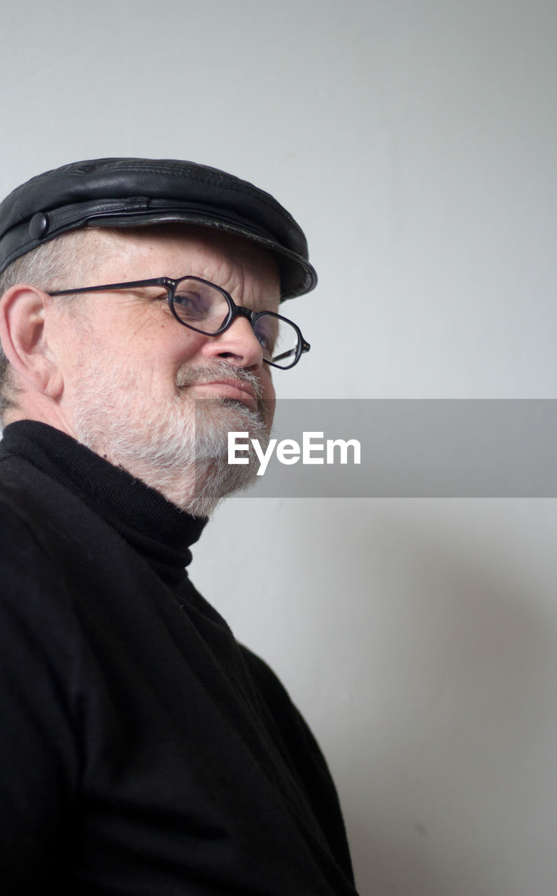 Close-up of senior man wearing flat cap and eyeglasses looking away at home