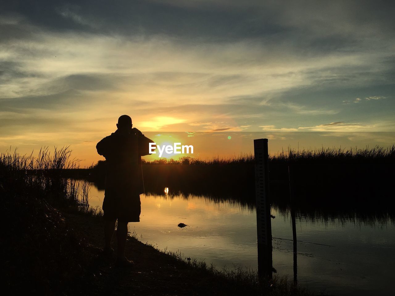 Silhouette man standing by lake against sky during sunset