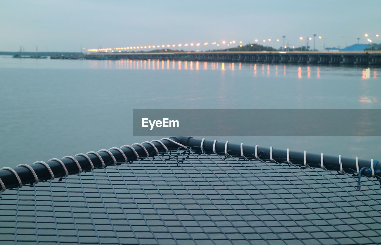 Closeup empty over-water hammock bed with blurry sea bridge in the backdrop