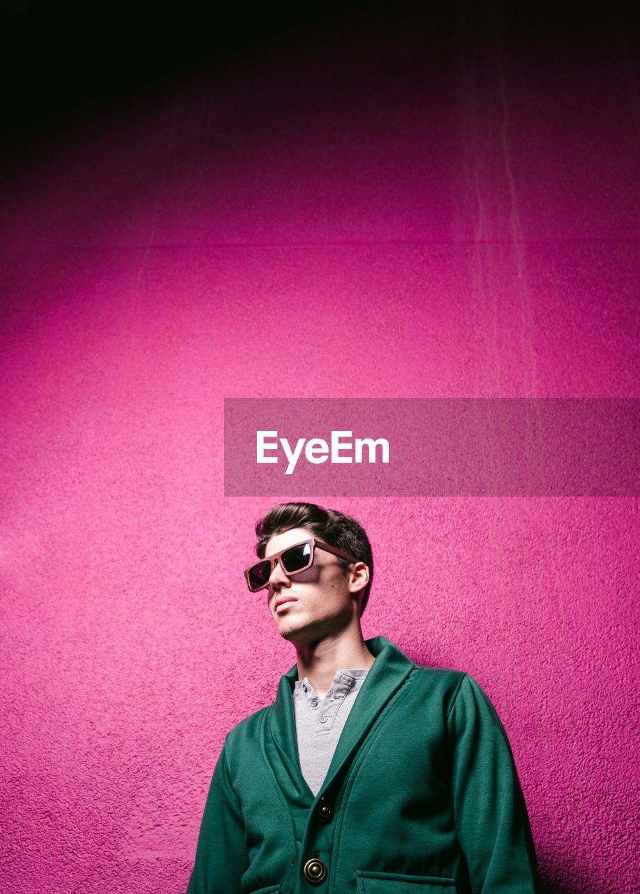 Man wearing sunglasses while standing against pink wall