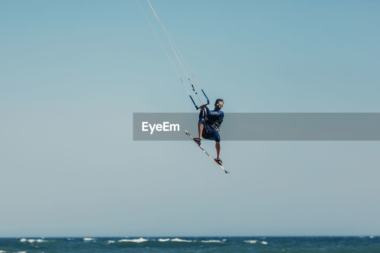 Mature man kiteboarding mid-air over sea on sunny day