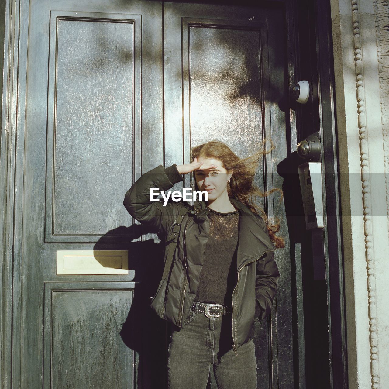 PORTRAIT OF YOUNG WOMAN STANDING AGAINST DOOR IN SNOW