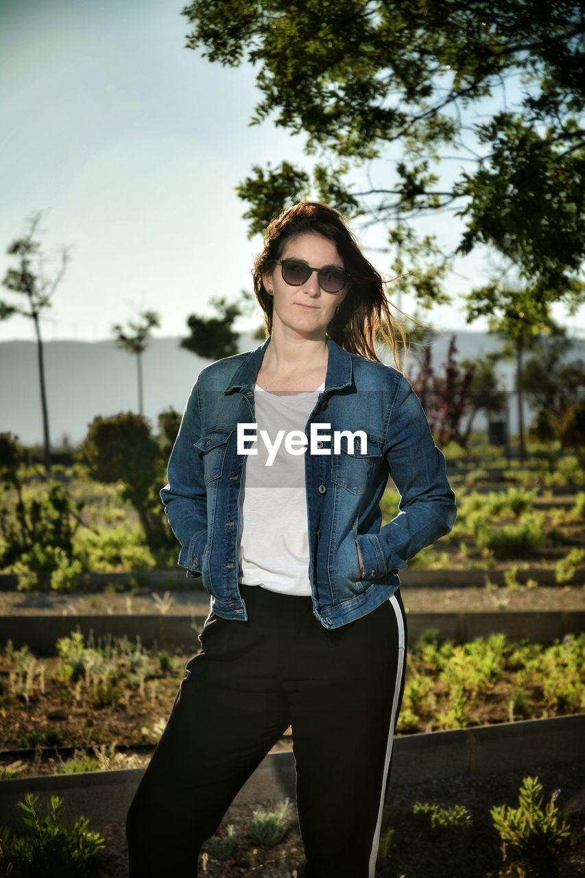 PORTRAIT OF YOUNG WOMAN STANDING BY TREES